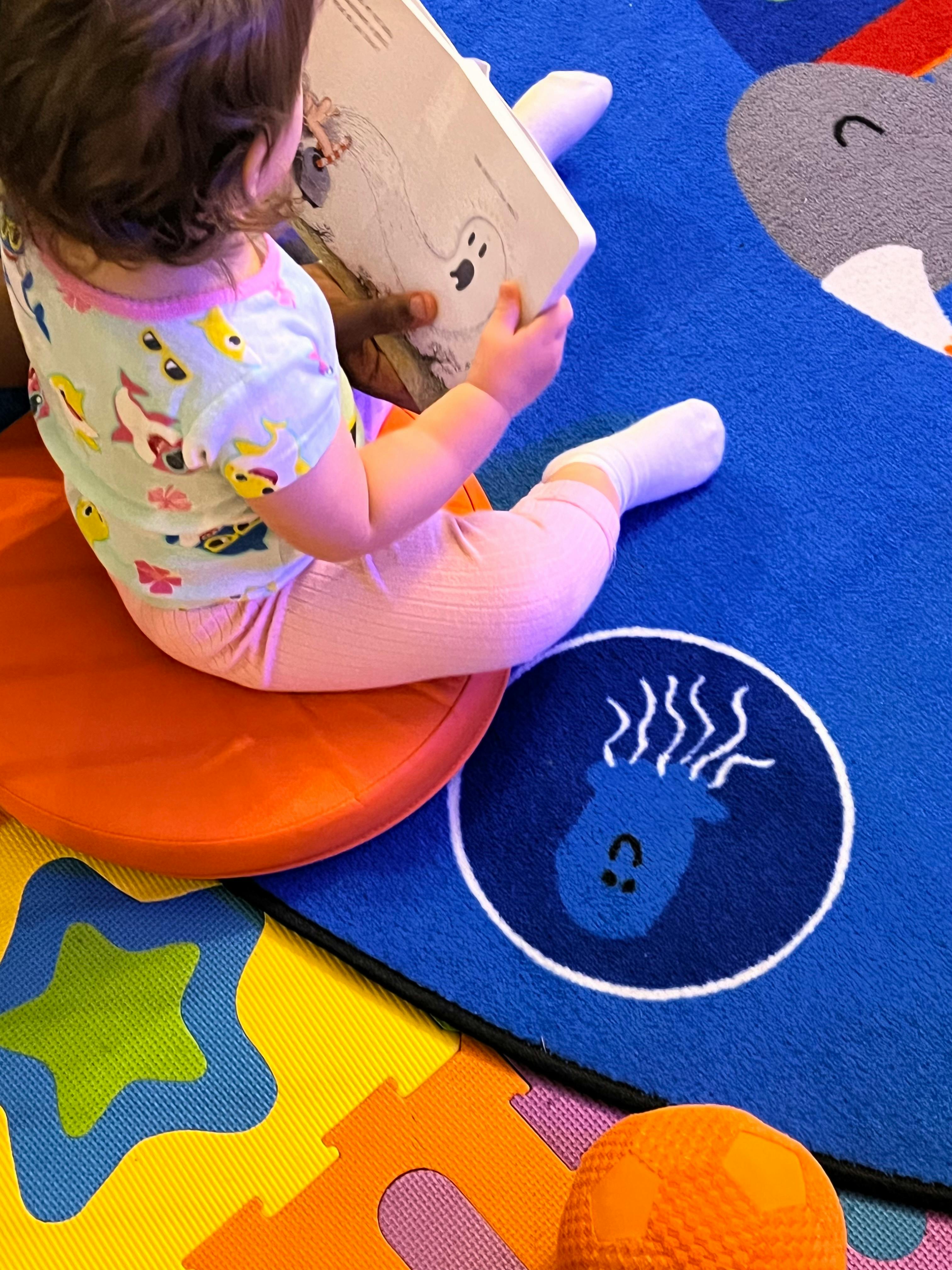 Child sitting on a cushion, holding a book