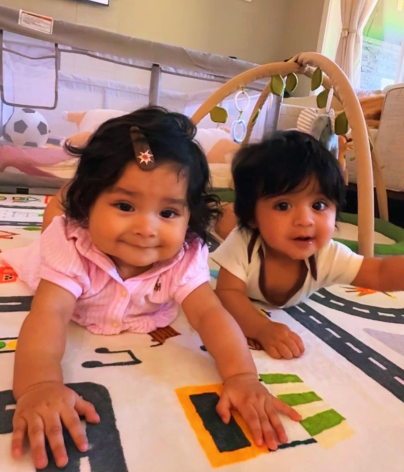 Two children lying on a play mat with a toy arch