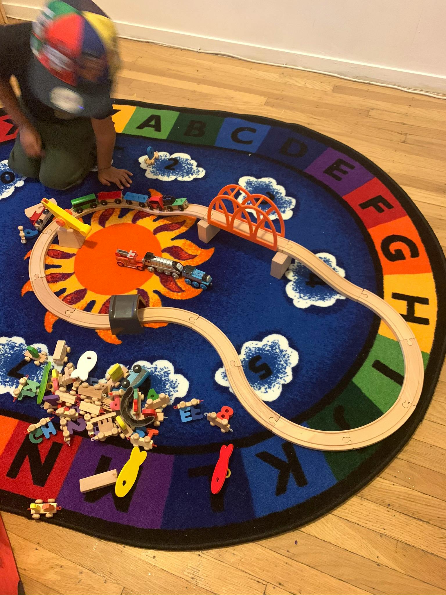 Child playing with a toy train set on an alphabet rug