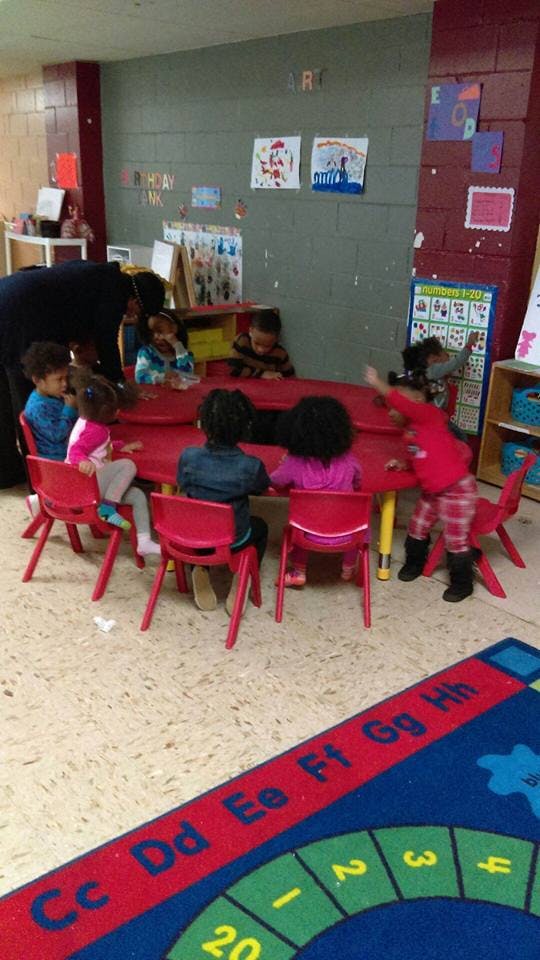 Adult and children gathered around a red table in a classroom