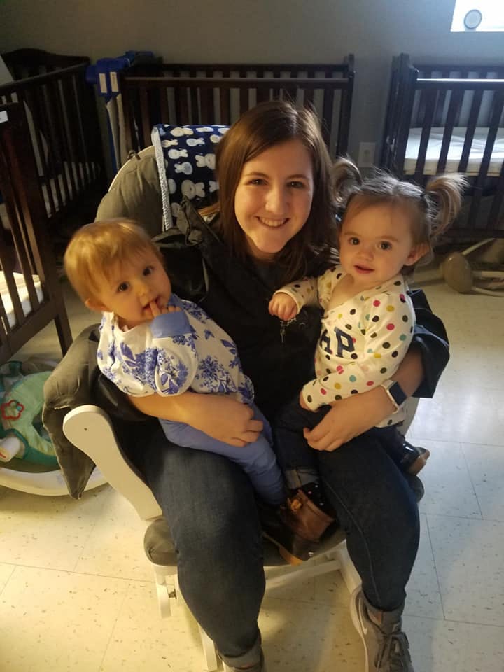 Person holding two children in a room with cribs