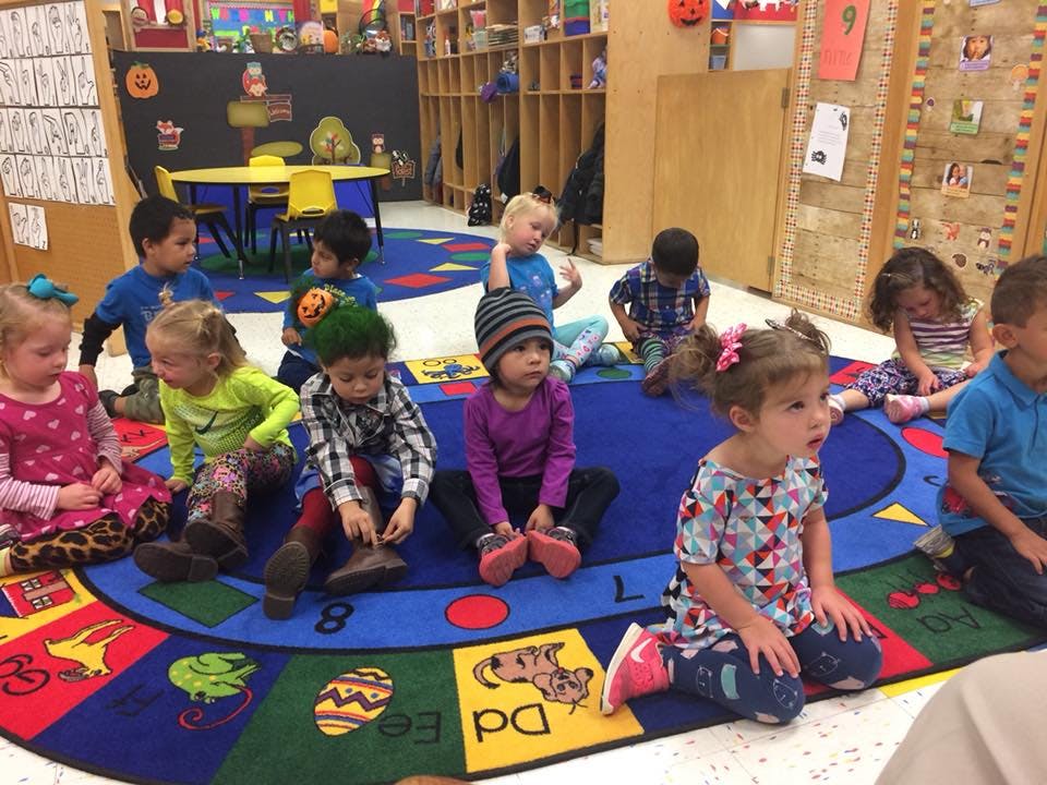 Group of children sitting on a colorful rug in a classroom