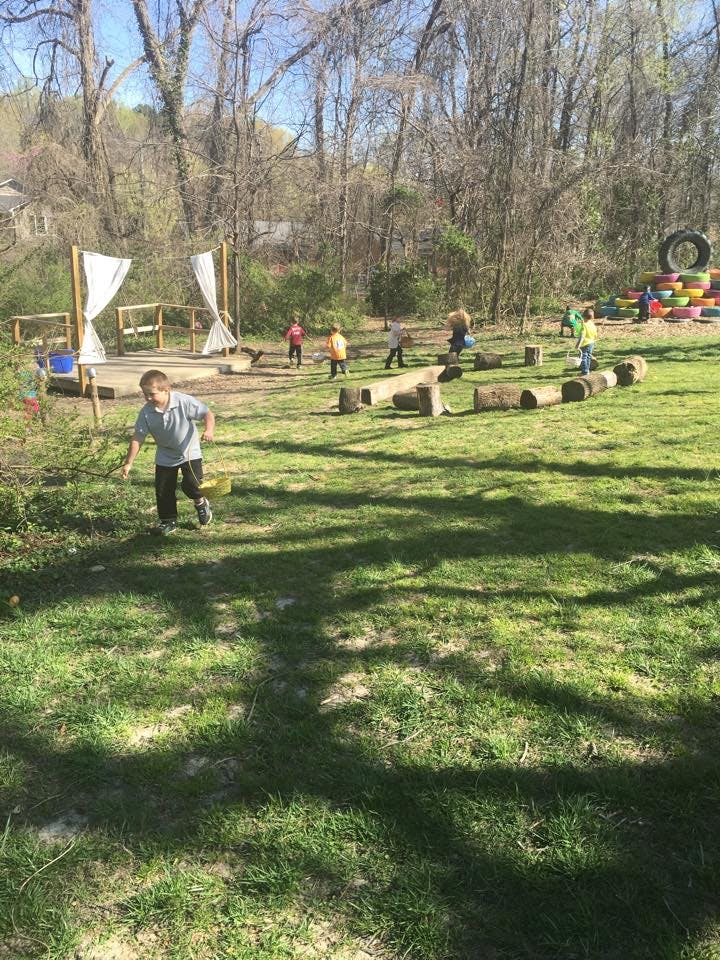 Child running in a grassy outdoor play area with other children and logs
