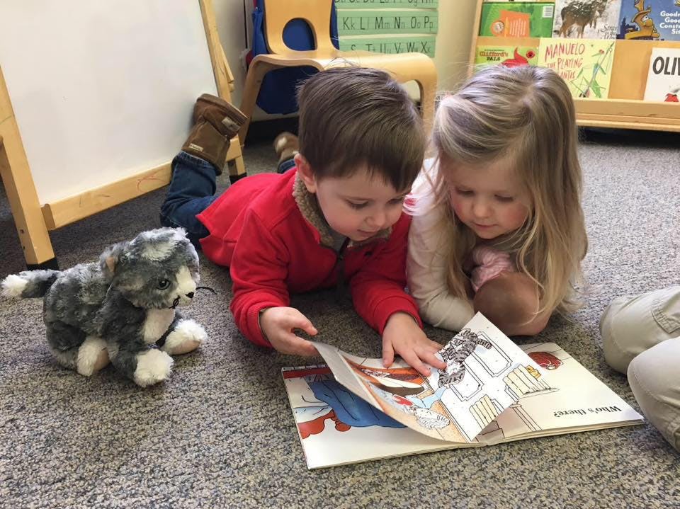 Two children lying on floor looking at a book