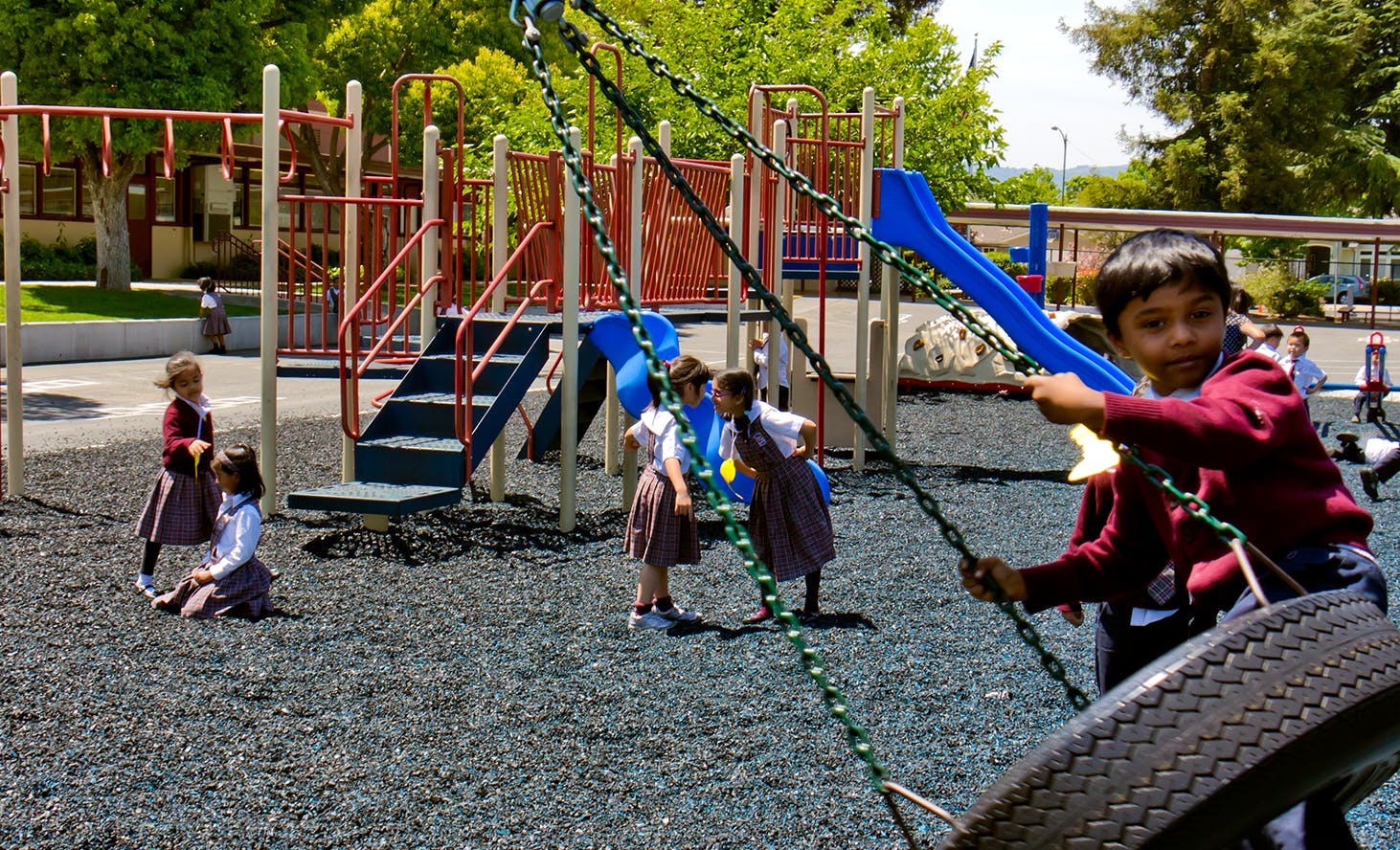 Child on a tire swing with other children and playground equipment