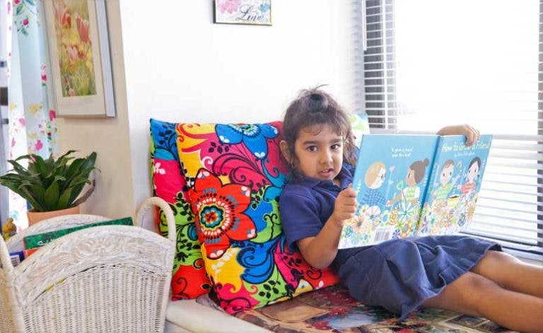 Child reading a book while leaning on a colorful pillow