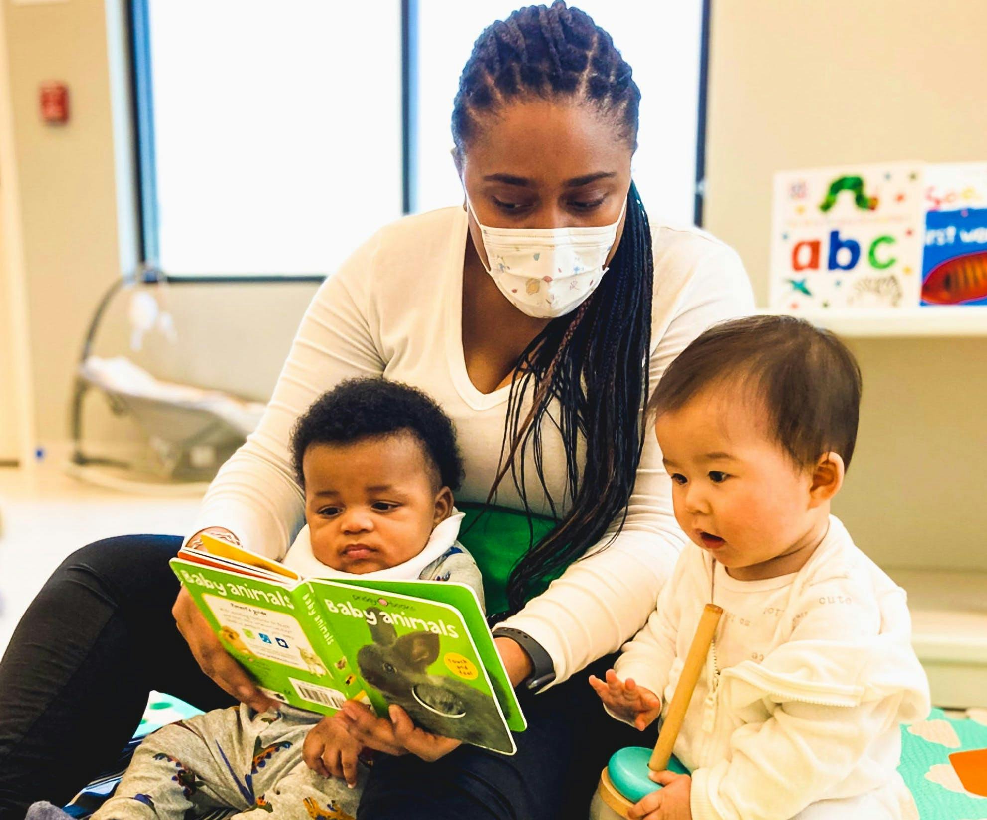 Person in mask reading a book to two children