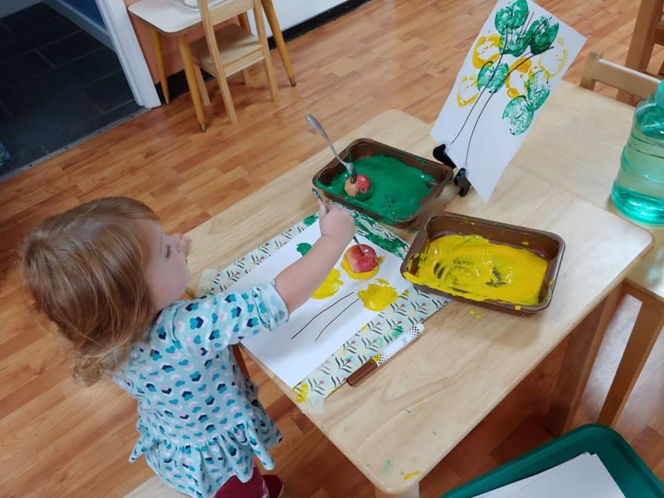 Child doing apple stamping art with green and yellow paint