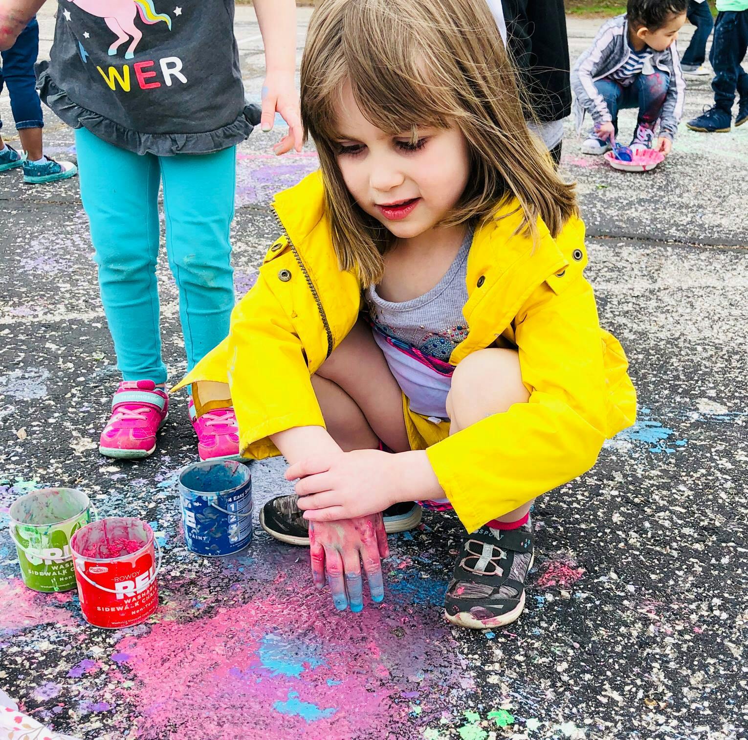 Child in yellow jacket playing with colorful chalk on the ground