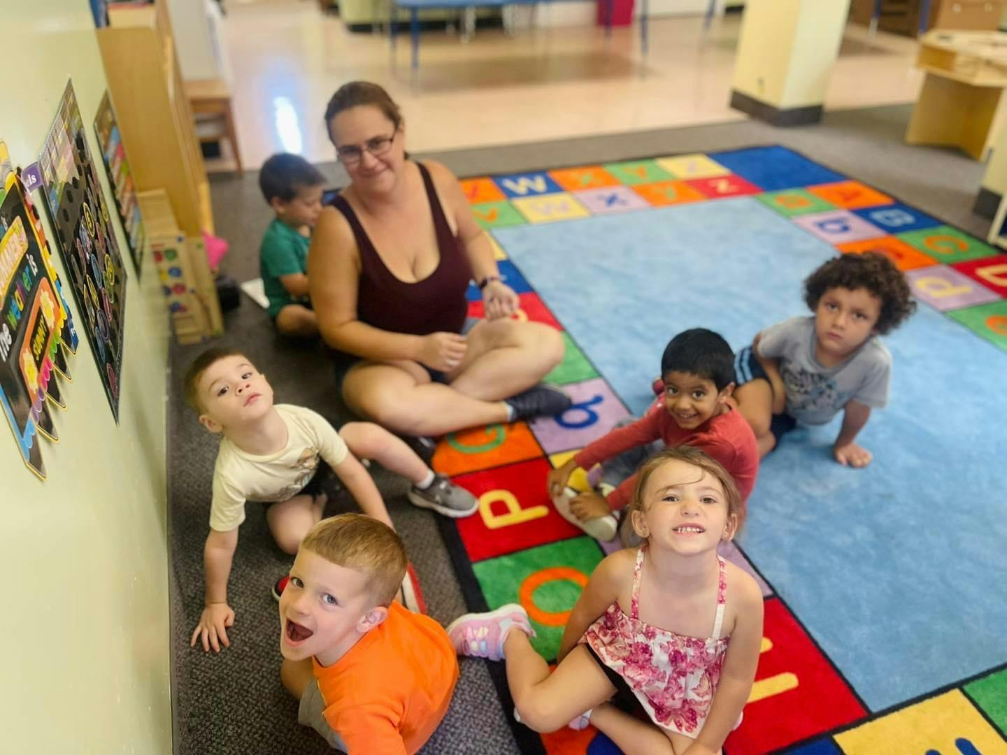 Adult and multiple children sitting on a colorful alphabet rug
