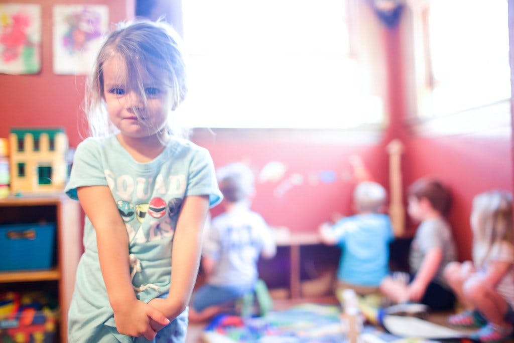 Child standing in a classroom with other children in the background