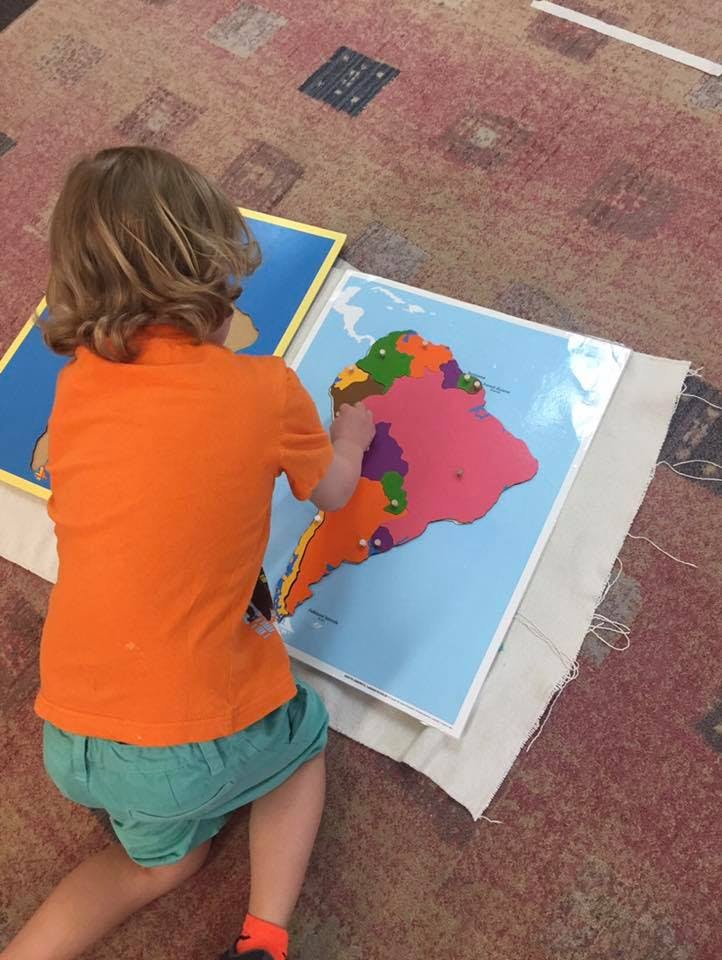 Child kneeling on floor working with a colorful puzzle map