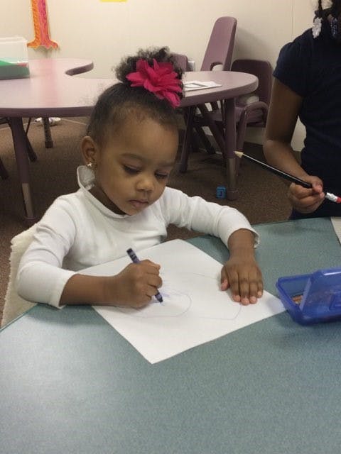 Child drawing on paper with a crayon at a table
