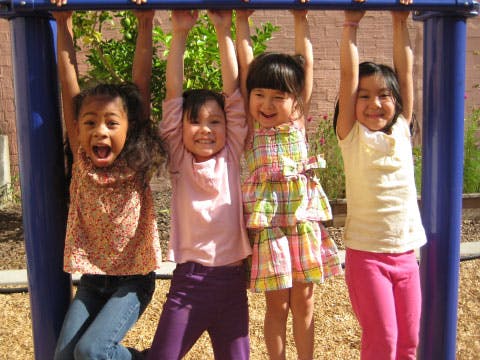 Four children hanging from monkey bars