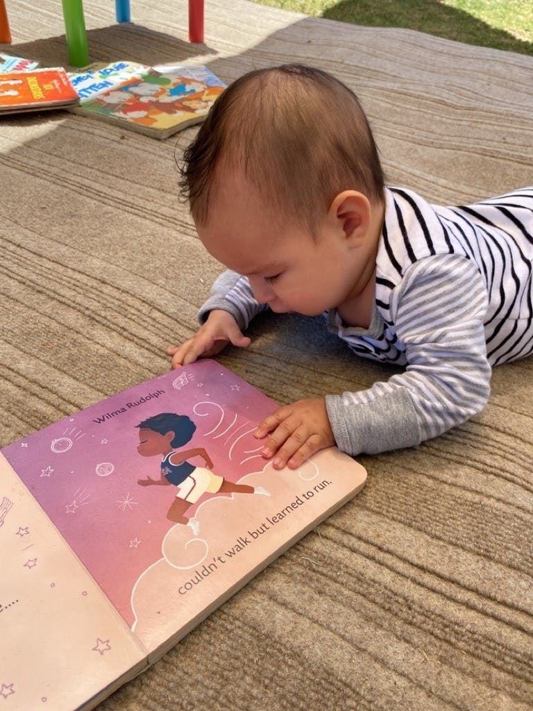 Baby on stomach looking at an open book with illustration of a running person
