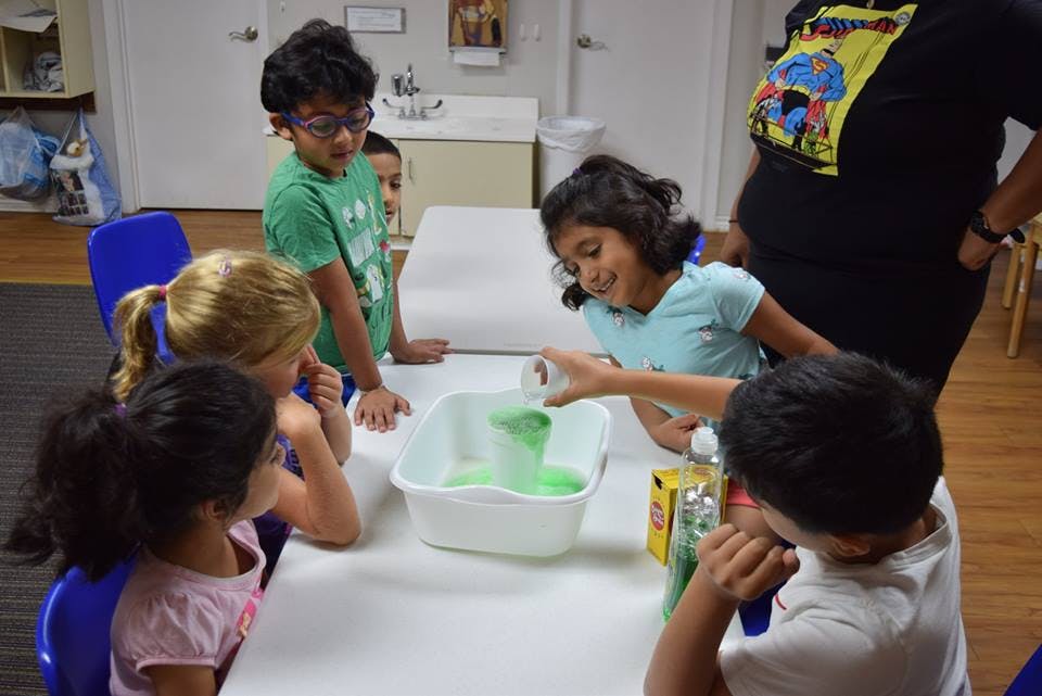 Children gathered around a table, one pouring liquid into a tub