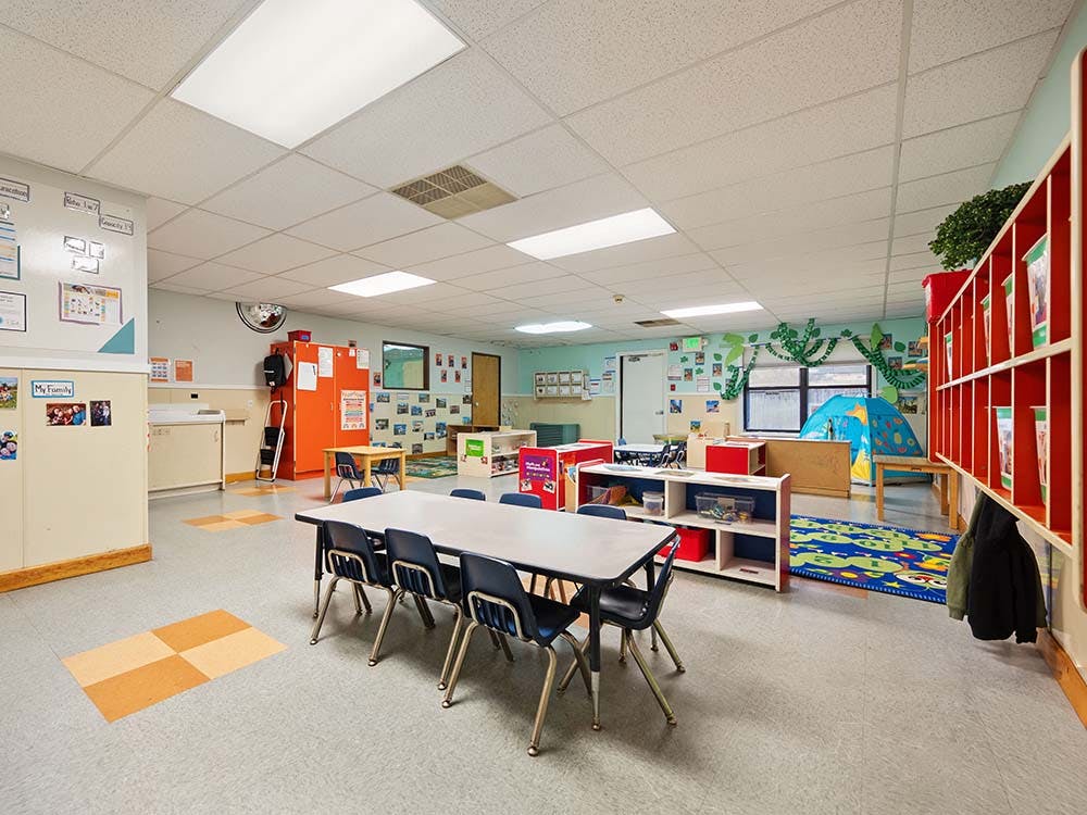 Empty colorful preschool classroom with small tables, chairs, and play areas