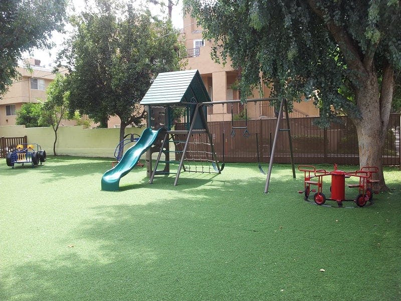 Playground with a slide, swings, and a small red table and chairs on artificial grass