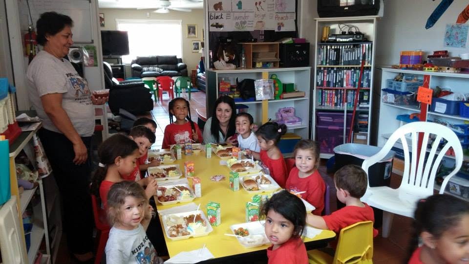 Adults and children sitting at a table with food containers