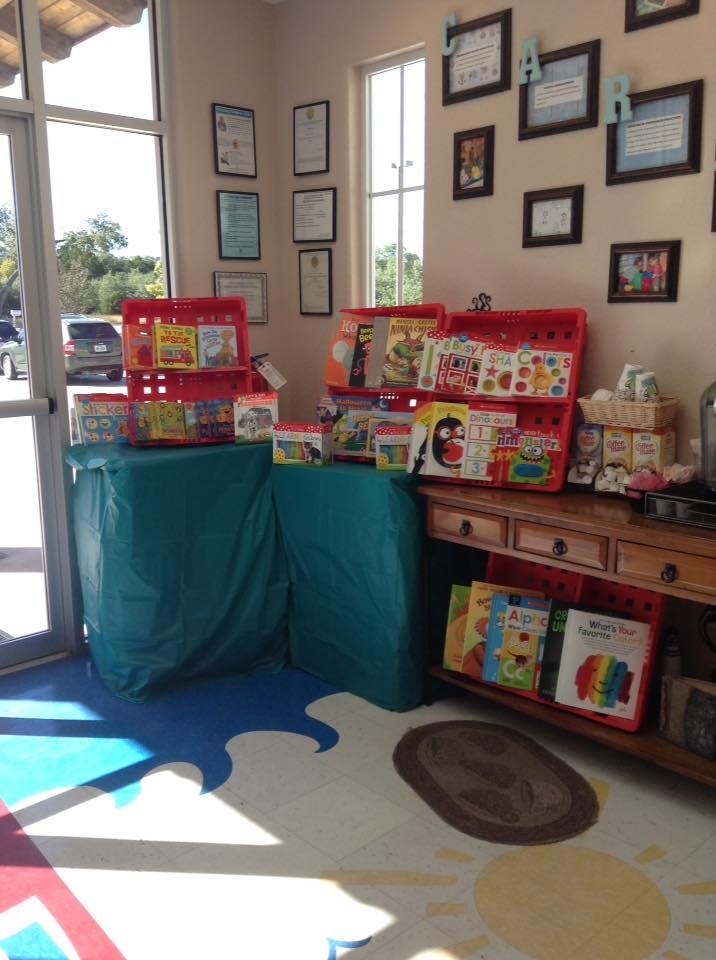 Books displayed in red bins on tables in a room with framed pictures