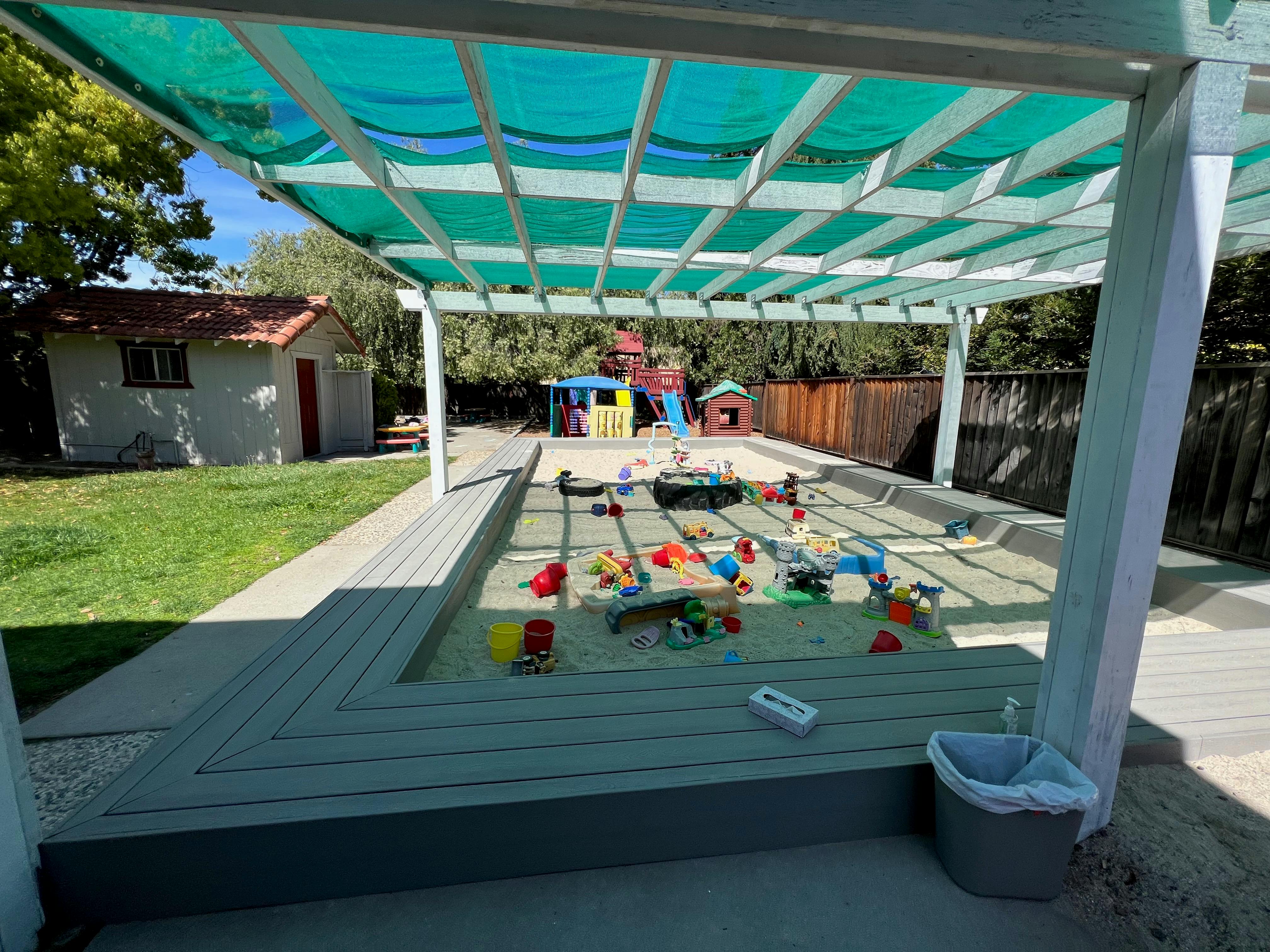 Outdoor sandbox with toys under a green shade structure