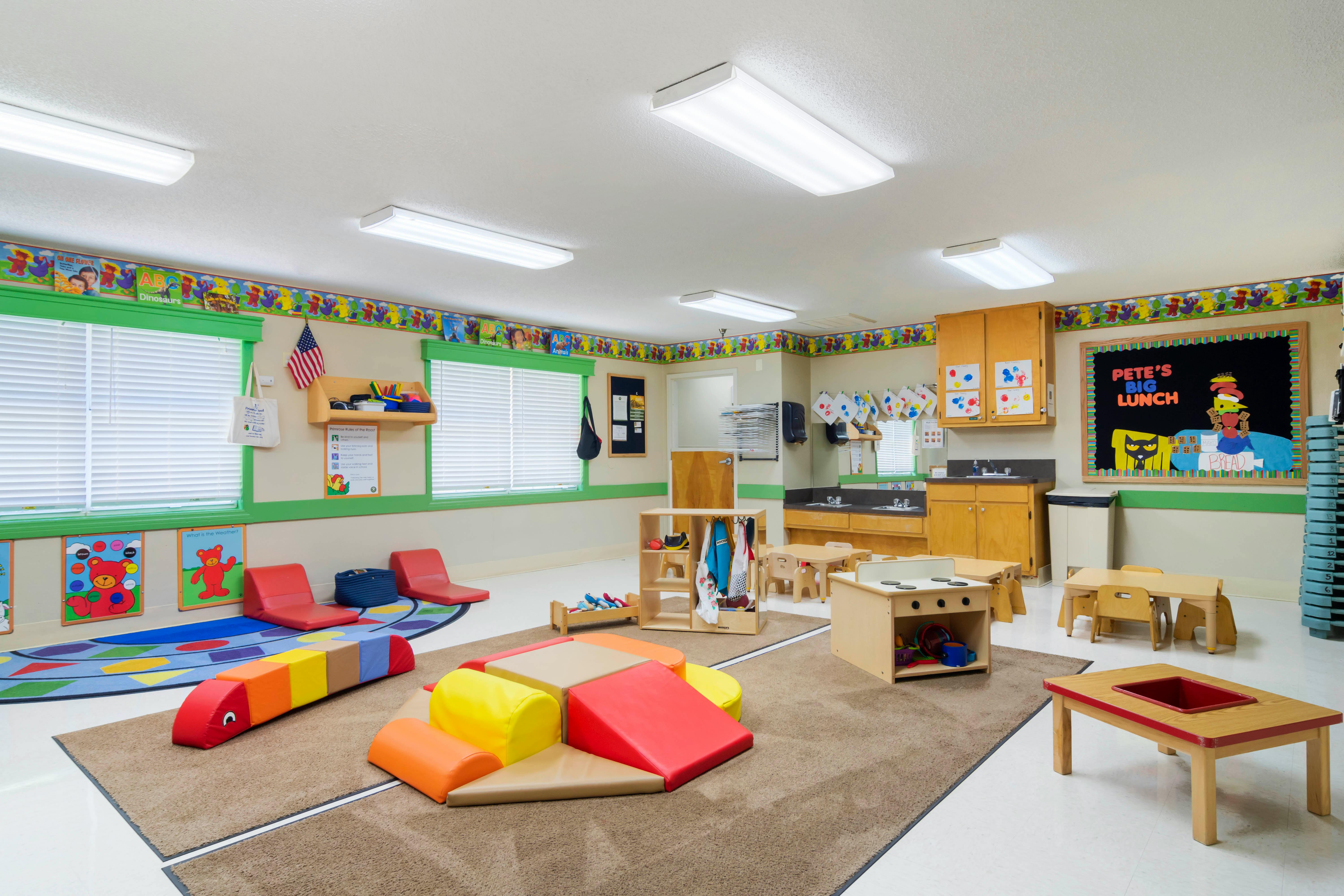 Classroom with colorful rugs, soft play blocks, small tables, and chairs