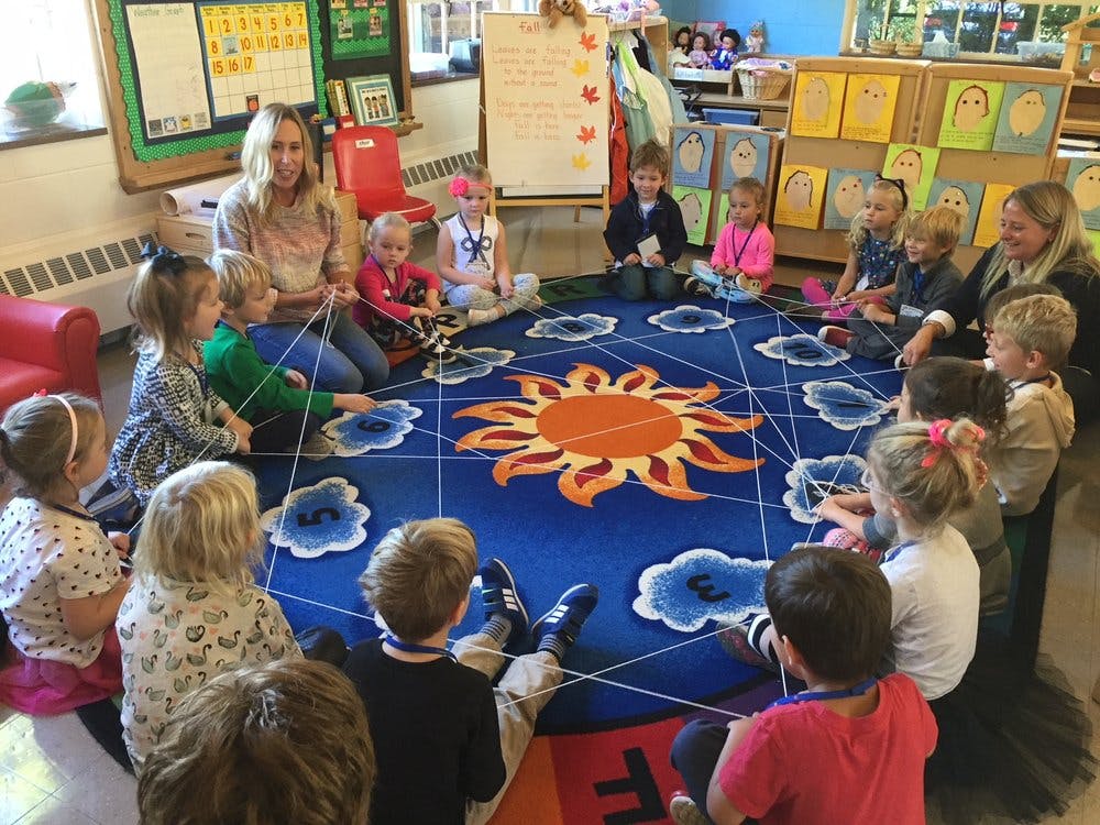 Adults and children sitting in a circle on a sun and clouds rug