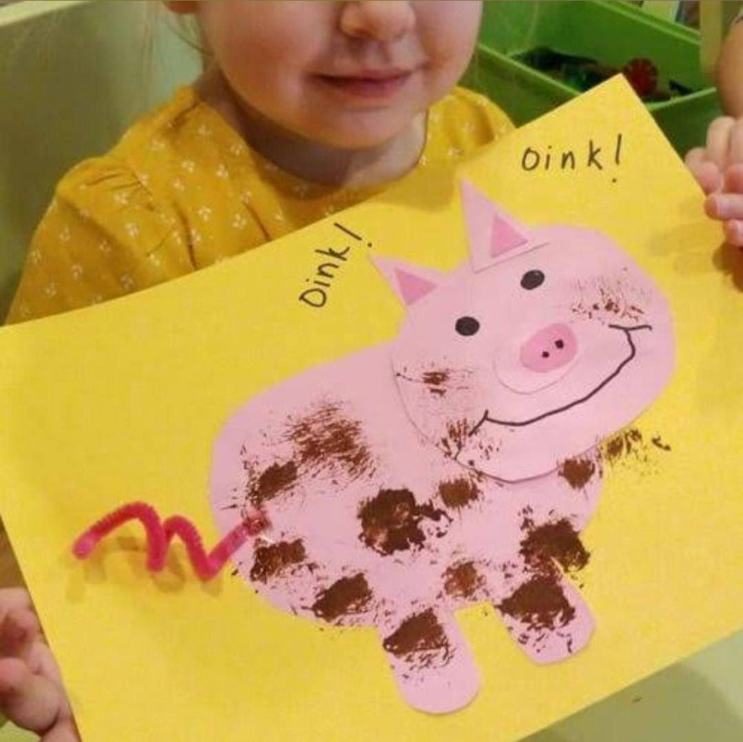 Child holding up a yellow paper craft of a pink pig with brown spots
