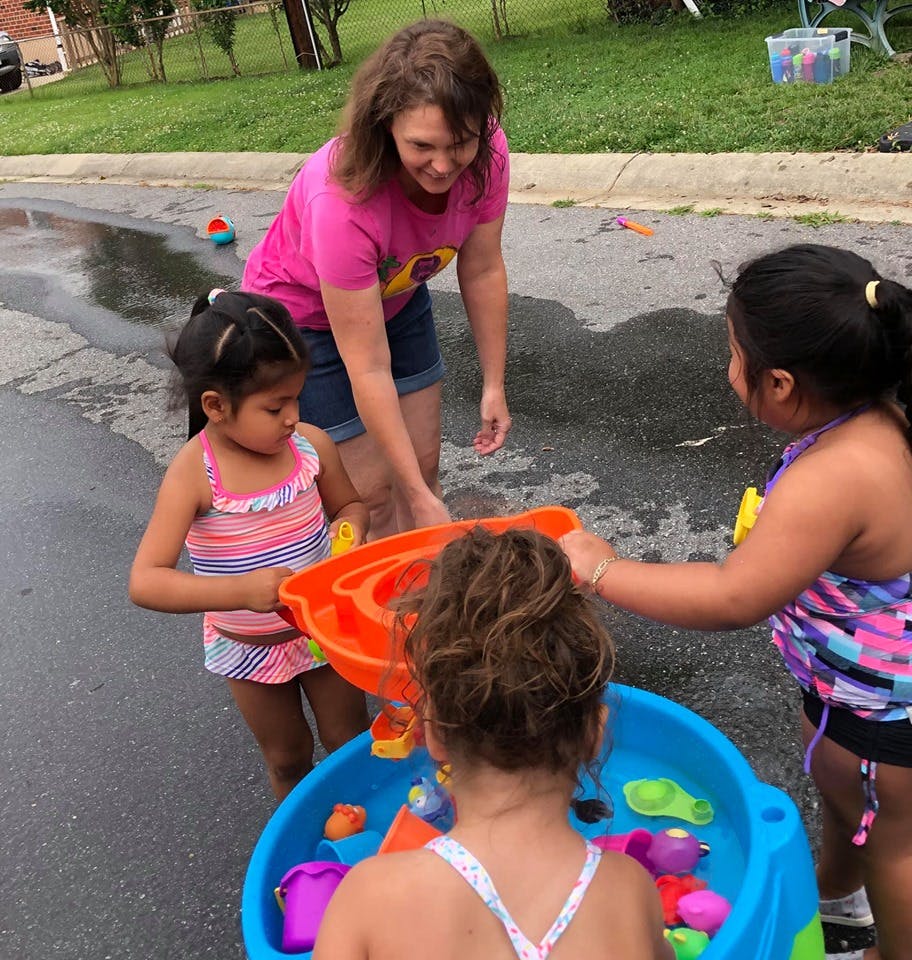Adult and three children playing with a water table outdoors