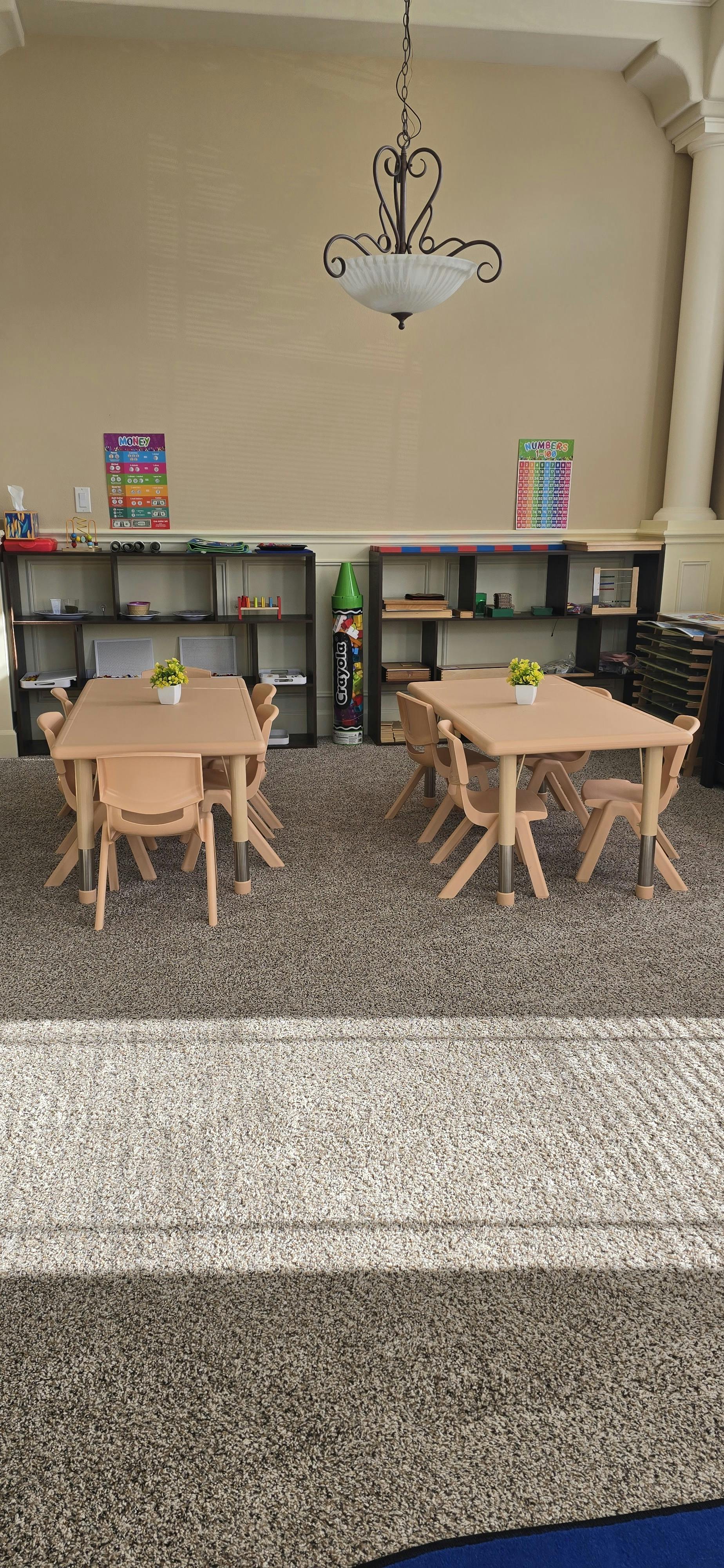 Classroom with child-sized tables and chairs, shelves with educational materials