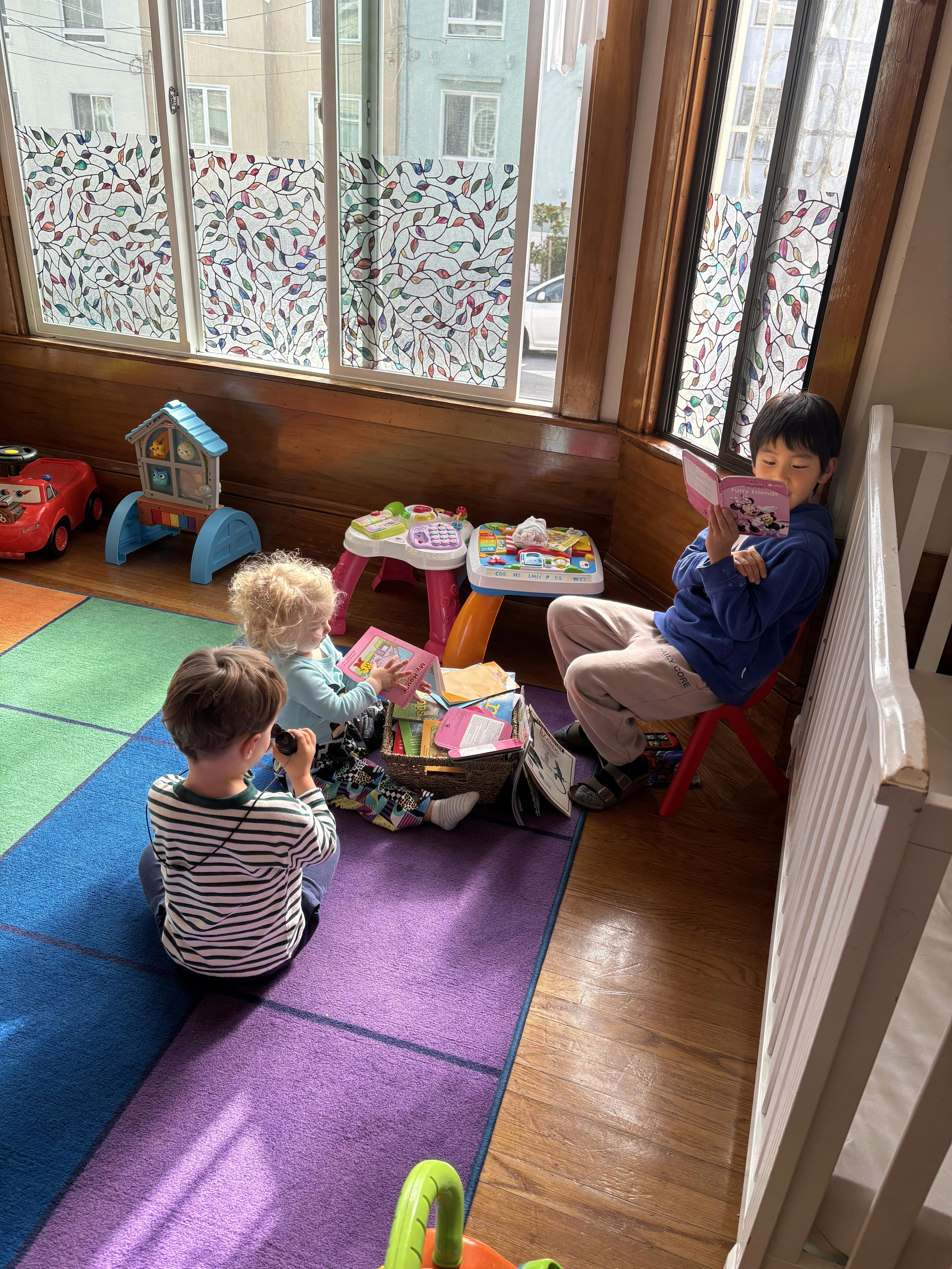 Three children playing and reading books on a colorful floor mat