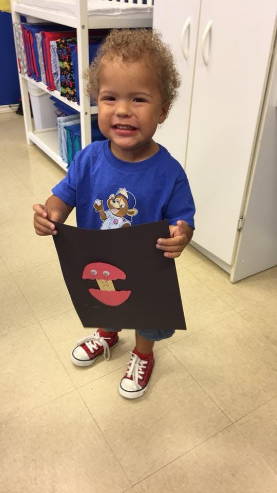 Child holding up a piece of paper with a mushroom drawing