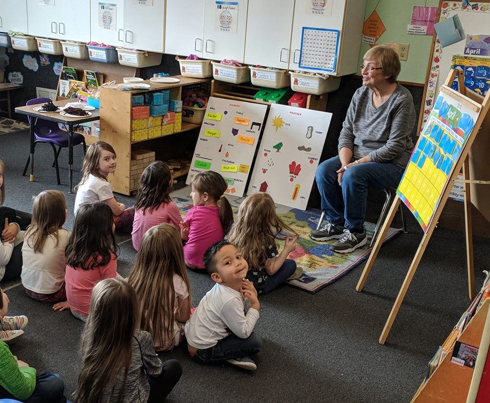 Adult person sitting on a chair with children sitting on the floor in a classroom