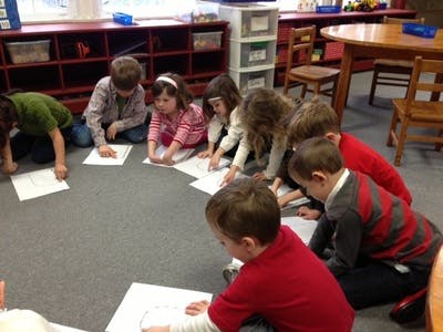 Children sitting on the floor drawing on paper in a classroom
