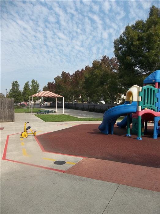 Empty playground with a yellow tricycle, blue slide, and striped canopy