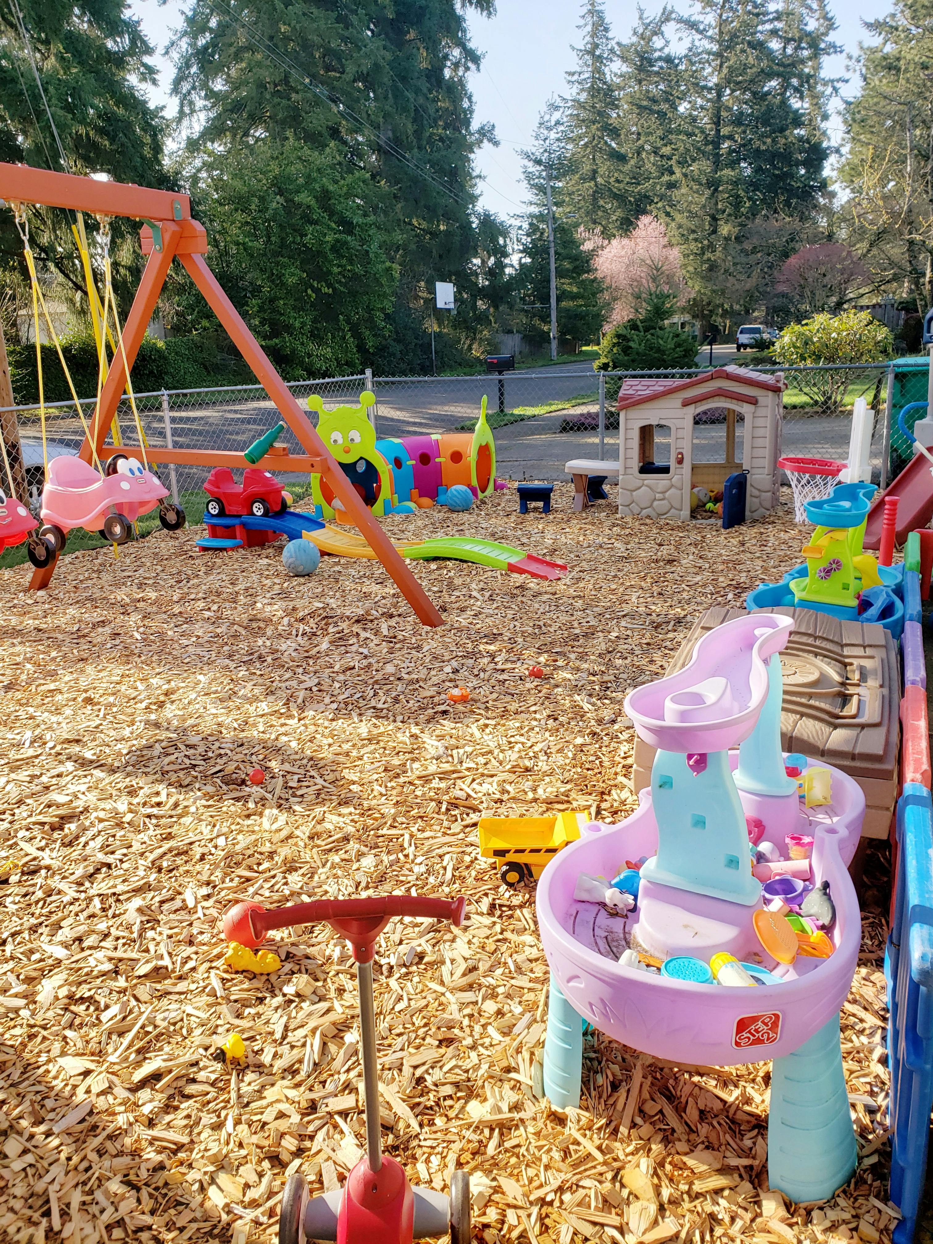 Outdoor playground with swings, playhouse, and various toys on wood chips