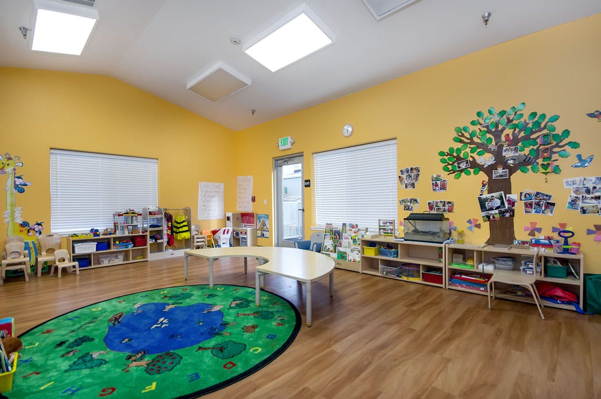 Classroom with yellow walls, a green rug, and small tables