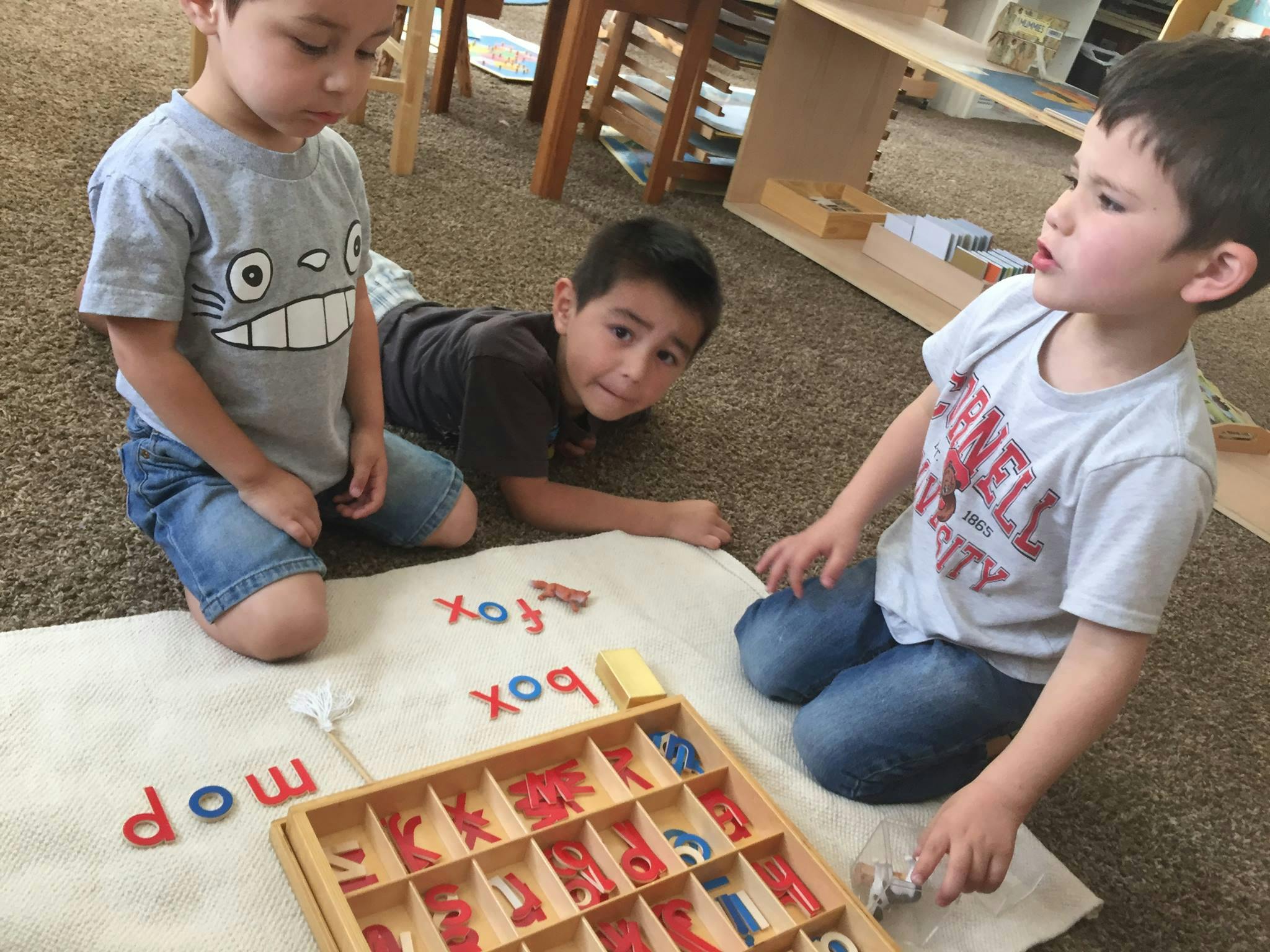 Three children on the floor with letter tiles spelling words