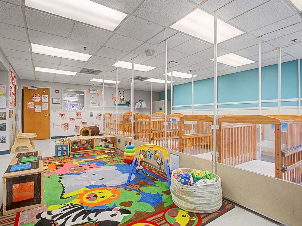 A classroom with a colorful rug, wooden cribs, and toys