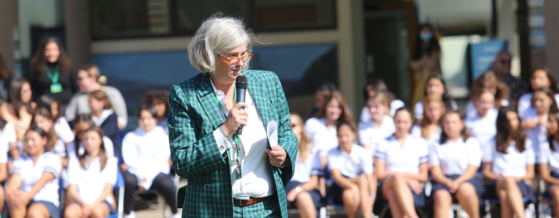 Person in a plaid jacket speaking into a microphone in front of a group of people