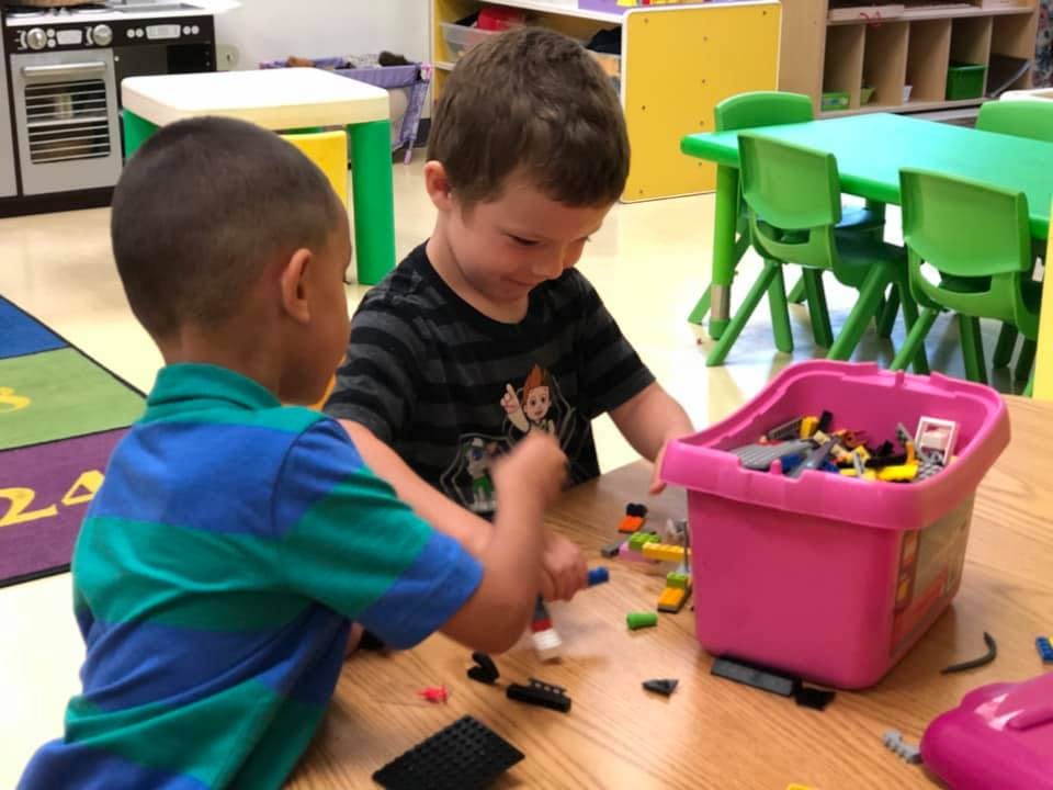 Two children playing with building blocks at a table in a classroom