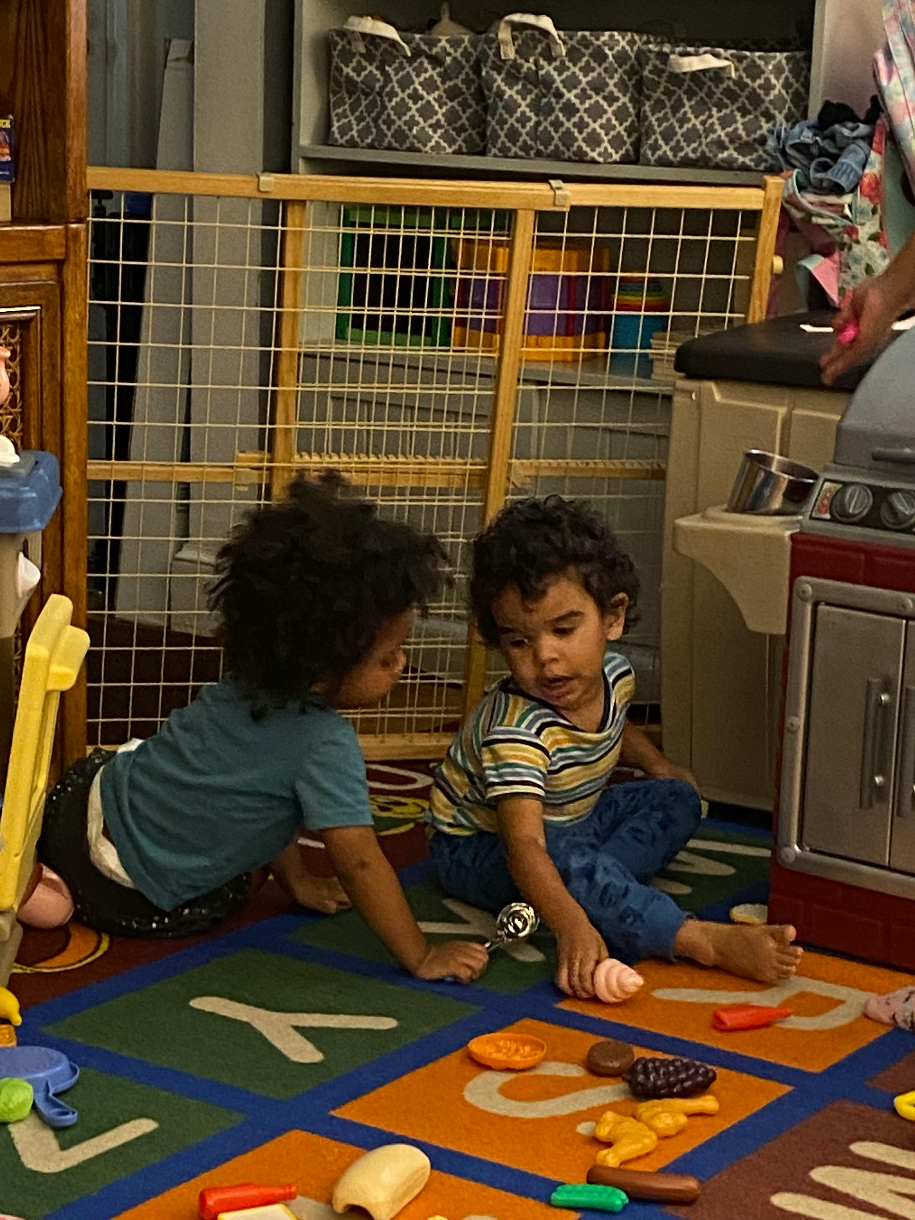 Two children playing on a rug with toys
