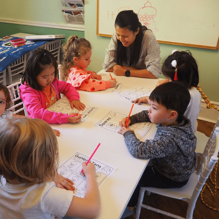 Adult and children drawing at a table in a classroom