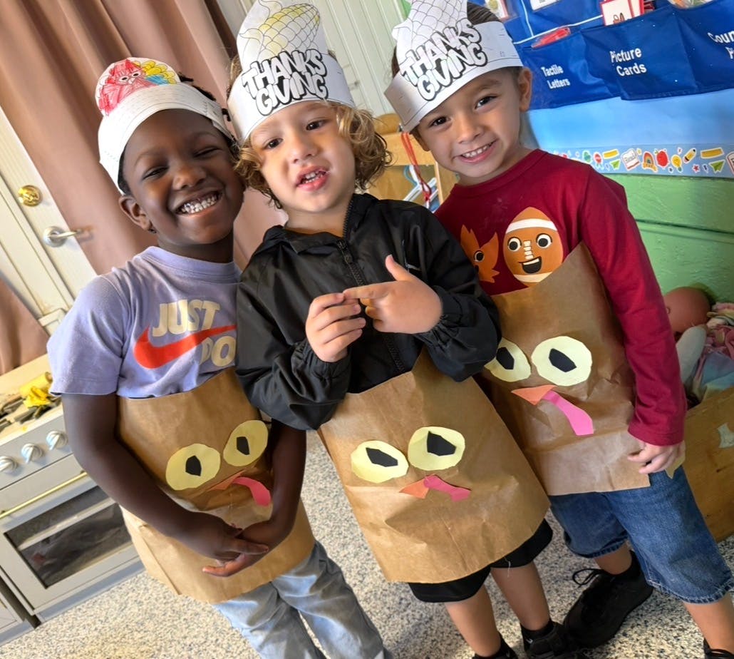 Three children in a classroom wearing turkey costumes and "Thanksgiving" hats