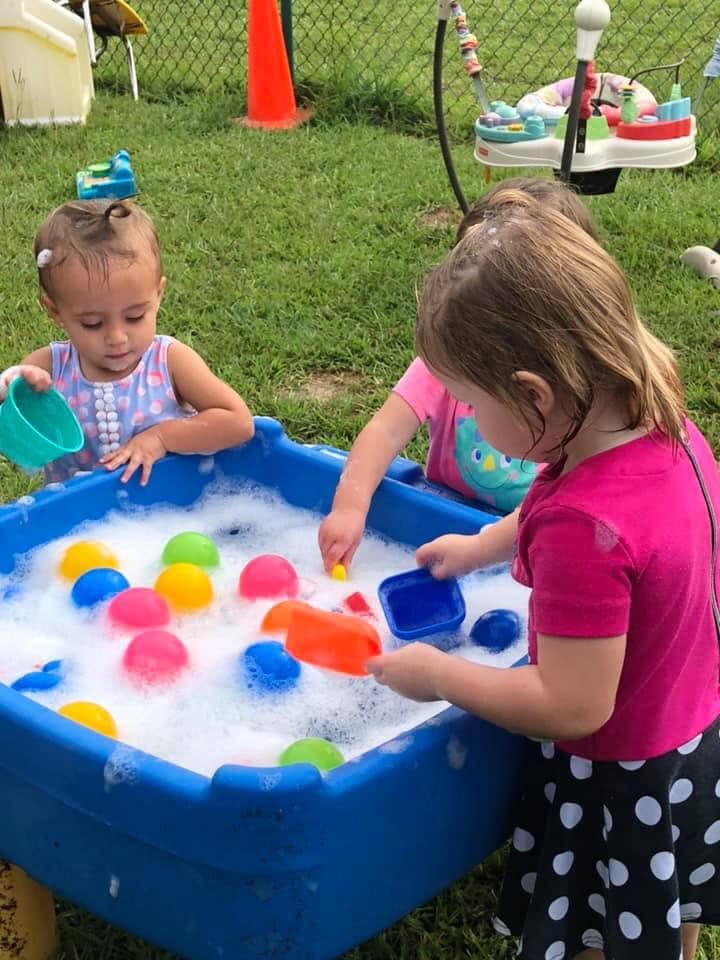 Two children playing with colorful toys in a bubbly water table