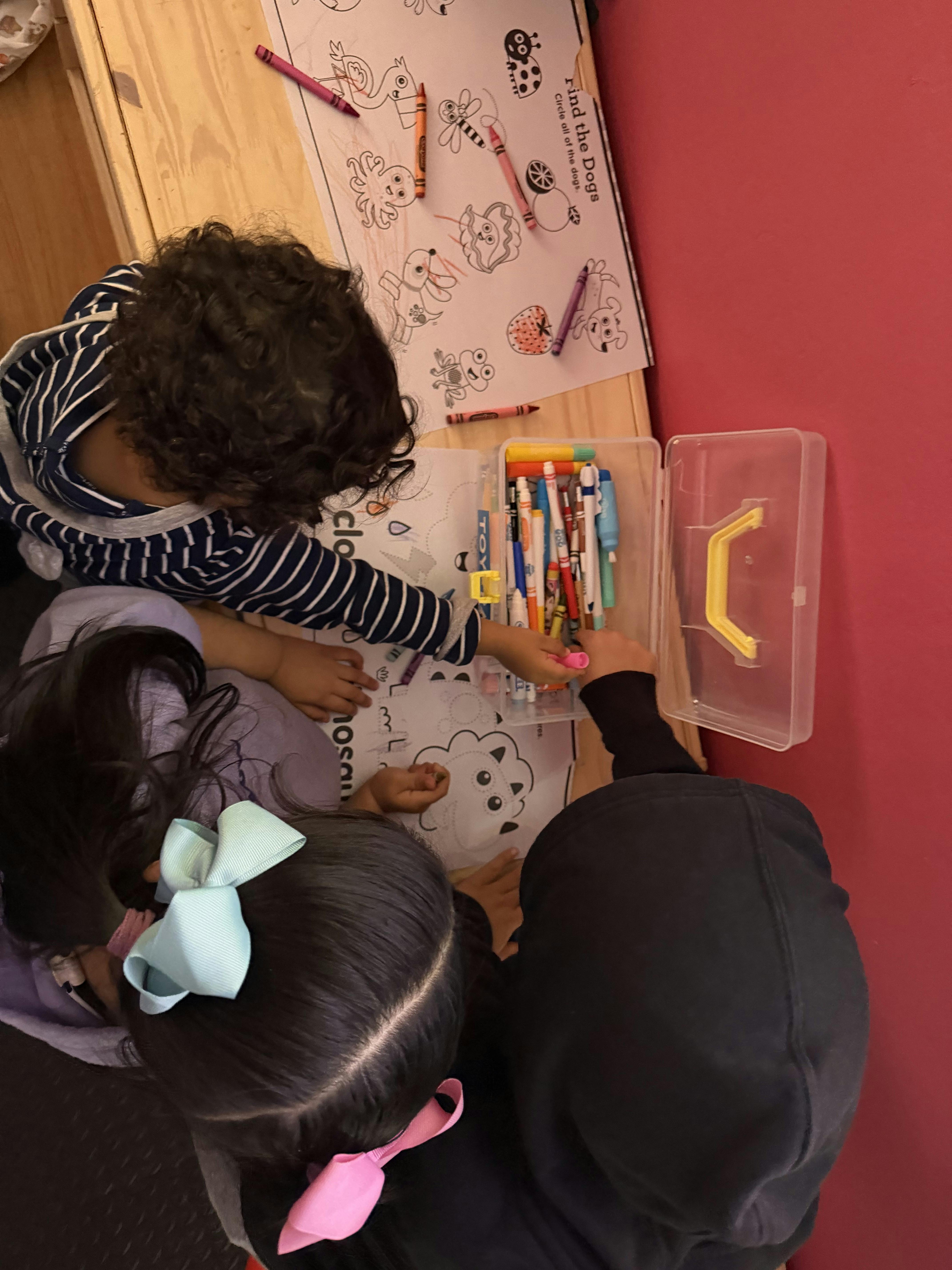 Three children drawing on coloring pages at a table