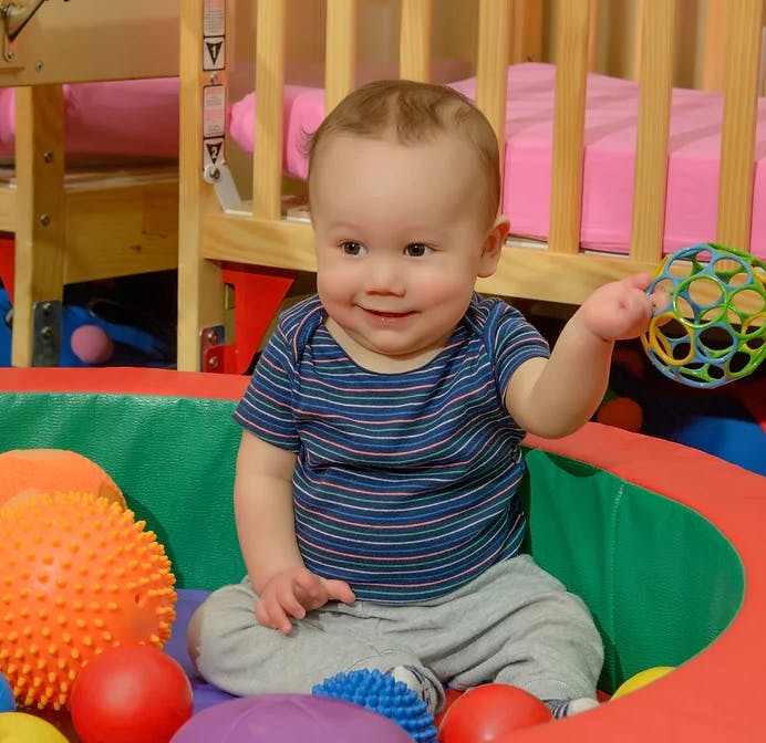 Child sitting in a playpen with toys, holding a colorful ball