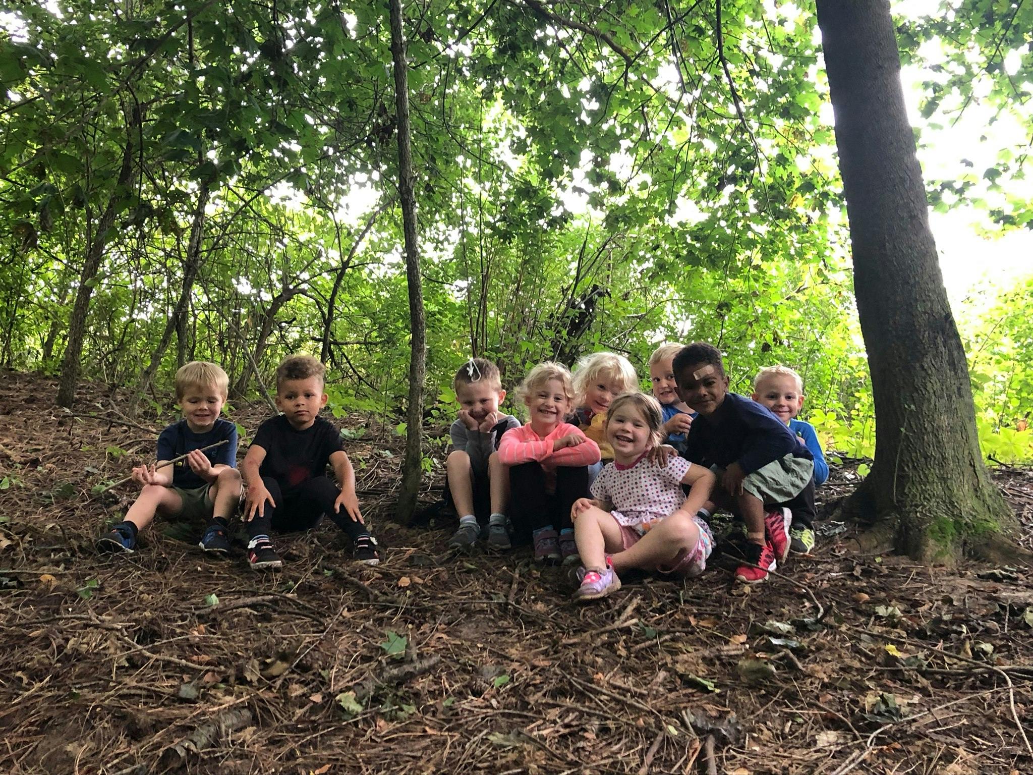 Group of children sitting on the ground in a wooded area