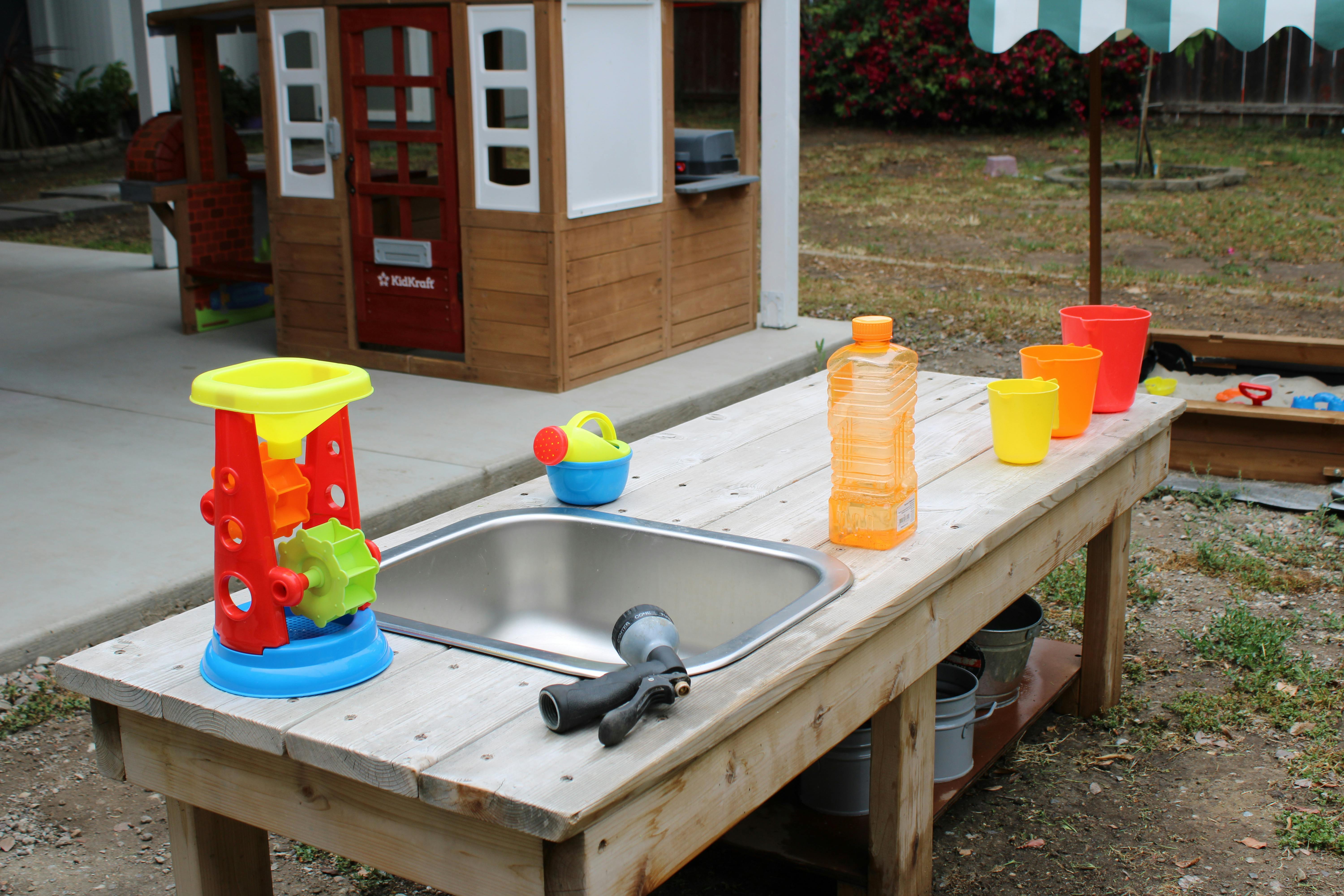 Outdoor play kitchen with a sink, water toys, and cups