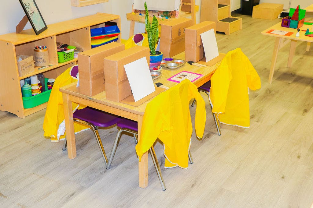 Classroom table with yellow smocks on chairs and cardboard boxes